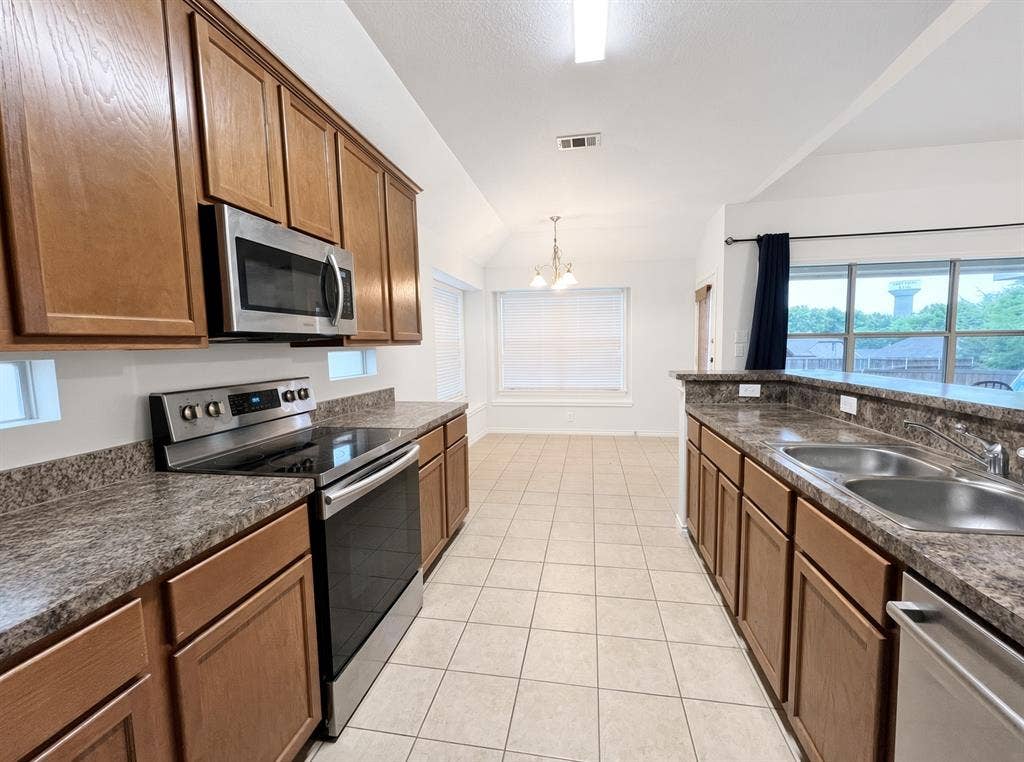 Kitchen featuring wood cabinetry, stone-patterned countertops, stainless steel appliances, and tile flooring