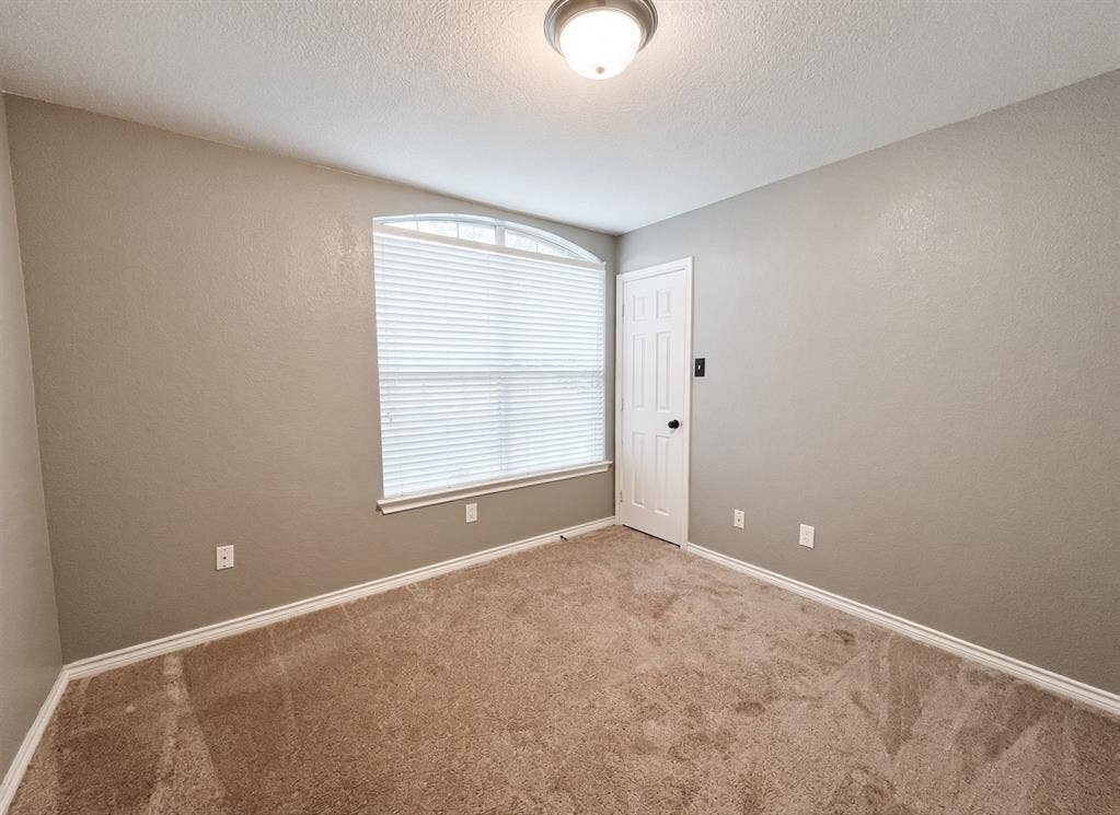 Neutral interior space featuring carpeted flooring, a six-panel door, and an arched window with horizontal blinds