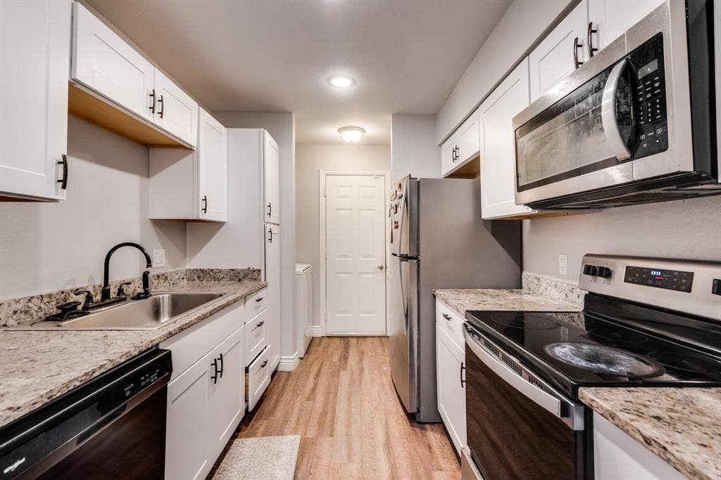 Kitchen featuring white shaker-style cabinetry, granite countertops, stainless steel appliances, a black gooseneck faucet.