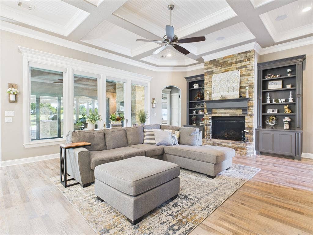 1201 E Iberian Court, Granbury, TX 76048 Coffered ceiling with beadboard detailing, floor-to-ceiling stone fireplace with custom mantel, and dark-finished built-in shelving