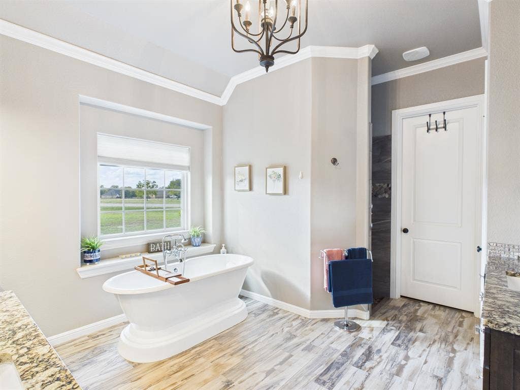 1201 E Iberian Court, Granbury, TX 76048 Freestanding soaking tub featuring chrome fixtures, wood-finish flooring, crown molding, multi-pane window, and iron chandelier