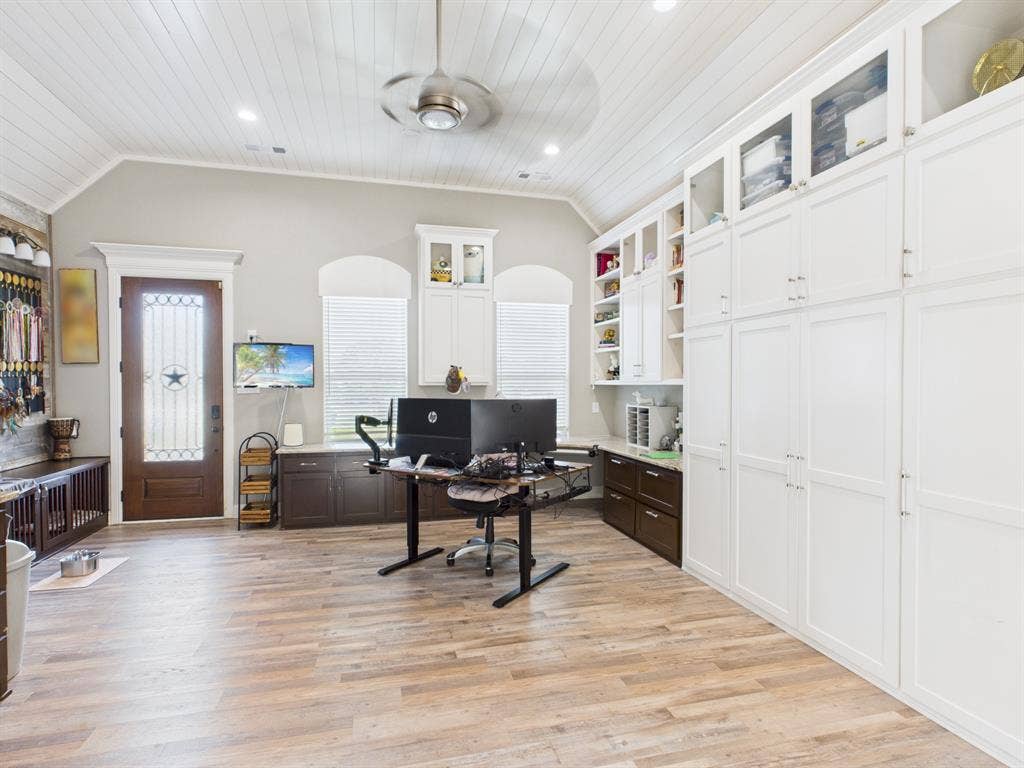 1201 E Iberian Court, Granbury, TX 76048 Vaulted ceiling with beadboard paneling, extensive floor-to-ceiling white cabinetry, wood-finish flooring, and a glass-paneled exterior door with arched window casing