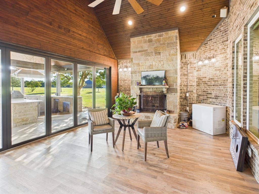 1201 E Iberian Court, Granbury, TX 76048 Covered outdoor living space featuring a vaulted tongue-and-groove wood ceiling, a floor-to-ceiling stone fireplace, brick wall accents, wood-finish flooring, and expansive multi-panel sliding glass doors