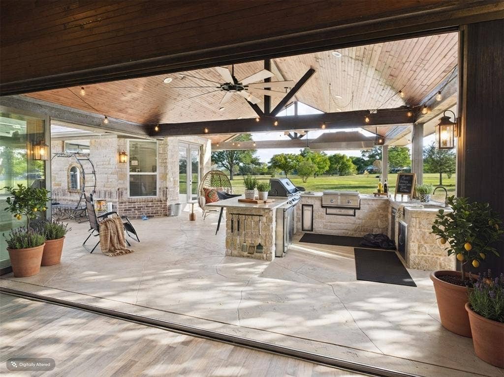 1201 E Iberian Court, Granbury, TX 76048 Covered outdoor living space featuring a stone-clad kitchen with integrated grill and sink, vaulted tongue-and-groove wood ceiling, stone tile flooring, and string lighting