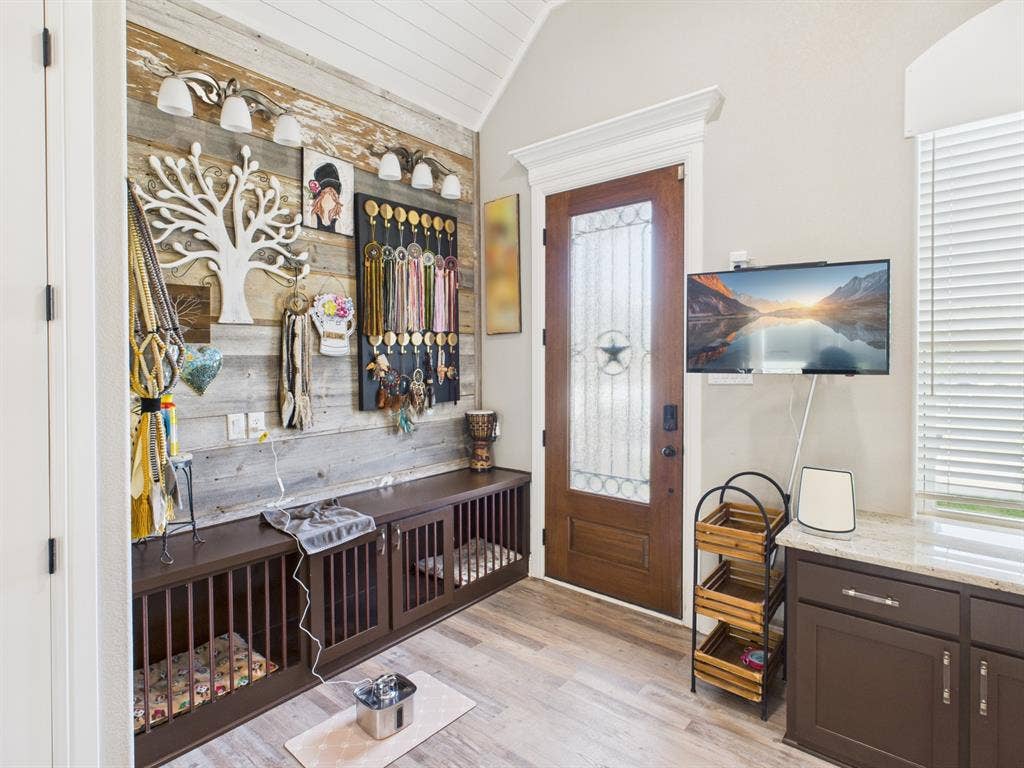 1201 E Iberian Court, Granbury, TX 76048 Reclaimed wood plank accent wall, built-in cabinetry featuring integrated kennel enclosures, stained wood door with decorative glass inlay, vaulted ceiling, and custom crown molding