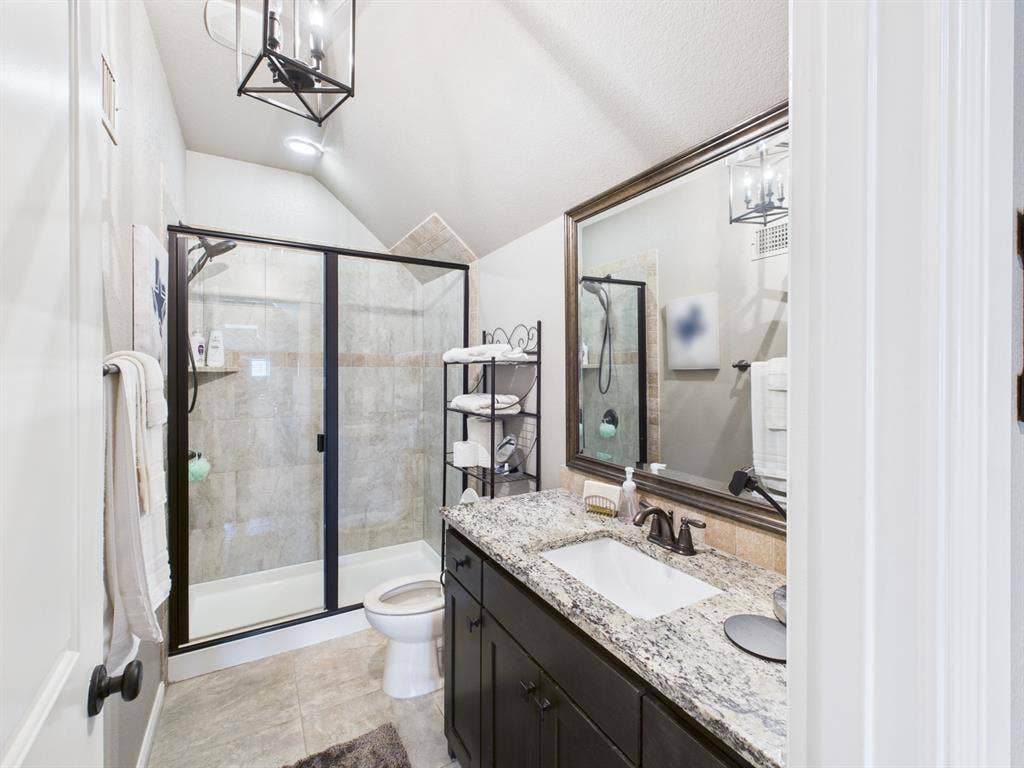 1201 E Iberian Court, Granbury, TX 76048 Bathroom featuring a dark wood vanity with stone countertop, undermount sink, shower with glass enclosure, and a geometric pendant light fixture