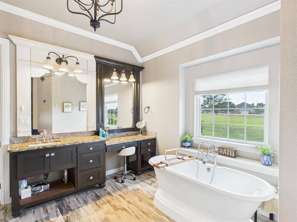 1201 E Iberian Court, Granbury, TX 76048 Custom dark wood vanity with stone countertop, freestanding soaking tub, multi-pane window, and decorative crown molding