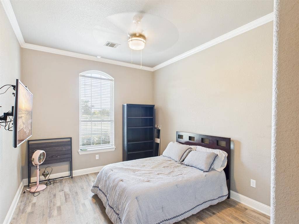 1201 E Iberian Court, Granbury, TX 76048 Neutral-toned interior featuring wood-finish flooring, crown molding, a central ceiling fan with integrated lighting, and an arched window