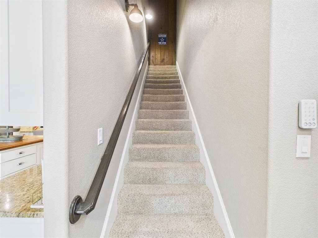 1201 E Iberian Court, Granbury, TX 76048 Staircase featuring wall-to-wall carpeting, a metal handrail, industrial-style wall sconce lighting, and a wood-panel door