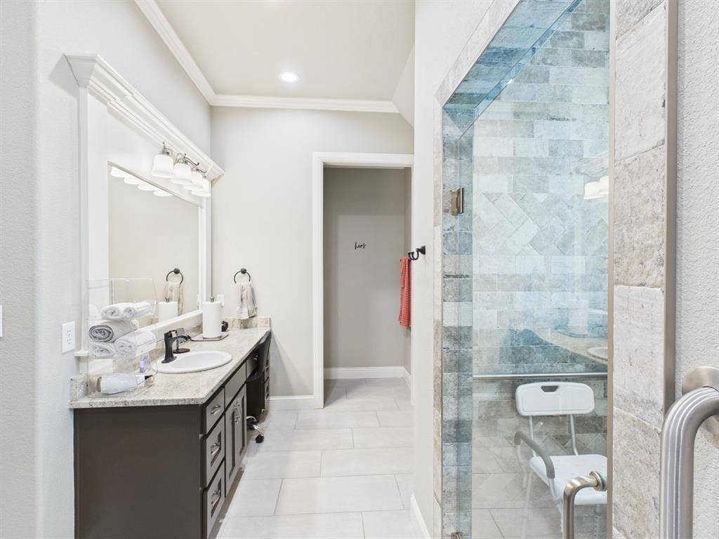 1201 E Iberian Court, Granbury, TX 76048 Bathroom featuring a vanity with stone-finish countertop, undermount sink, multi-light fixture, walk-in shower with tile surround, and large-format floor tile
