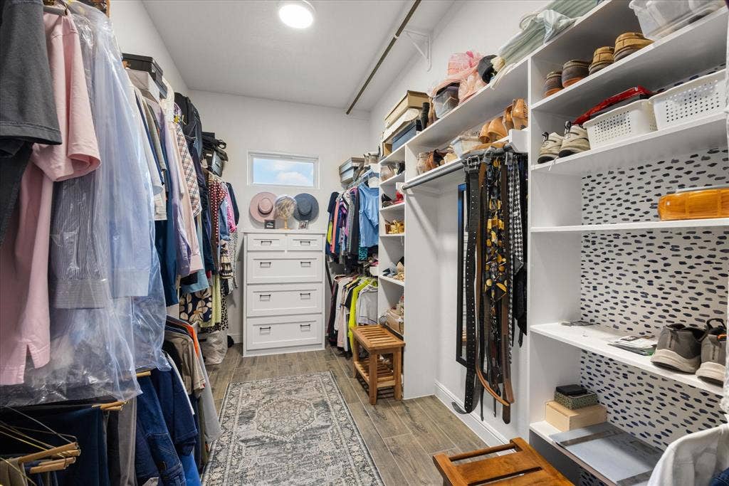 Walk-in closet featuring white built-in shelving, integrated hanging rods, wood-finish flooring, and a single transom window