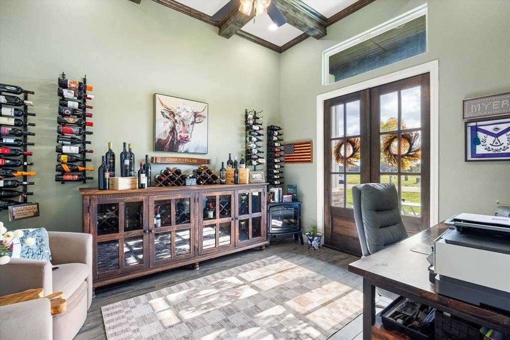 Vaulted ceiling with exposed wood beams, stained wood-finish double entry doors with transom window, built-in wooden cabinetry with glass paneling, and wall-mounted metal bottle storage racks