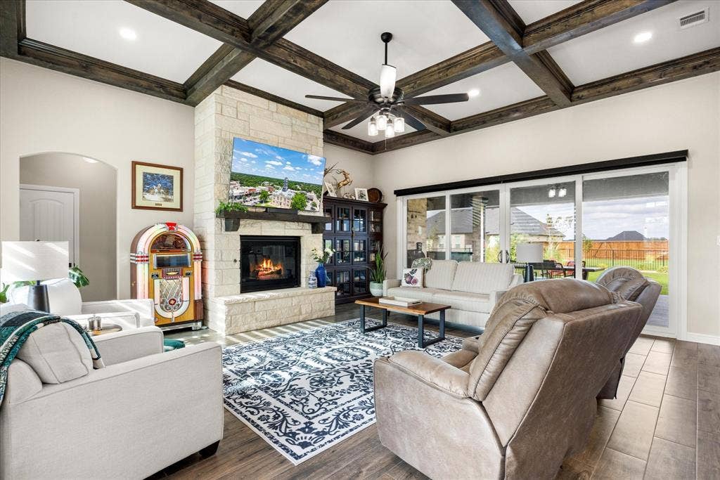 Coffered ceiling with dark wood-finish beams, stone-faced fireplace with a wood mantel, and sliding glass doors