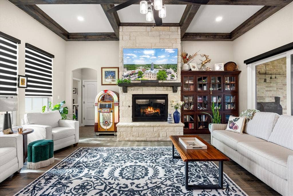 Living room featuring a floor-to-ceiling stone fireplace with a thick timber mantel, dark wood coffered ceiling beams, wood-finish flooring, and built-in dark wood cabinetry