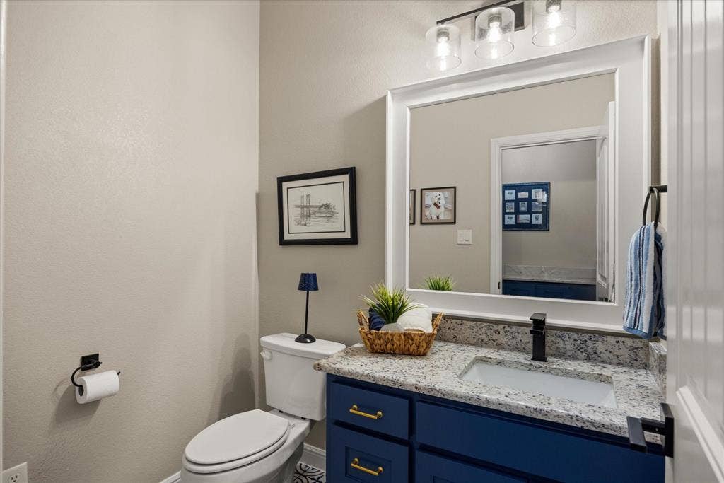 Vanity featuring a stone-composite countertop, undermount sink, matte black faucet, and navy blue cabinetry with gold-toned pulls, complemented by a large framed wall mirror and three-light glass fixture