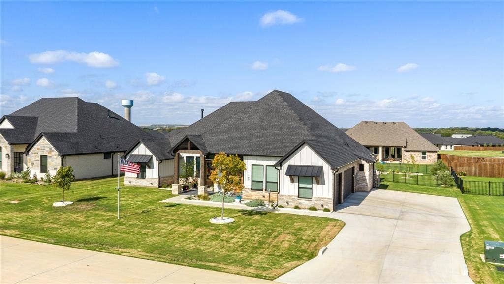 Exterior featuring a mix of stone and vertical siding, dark shingle roofing, metal window awnings, an integrated multi-car garage, and a concrete driveway