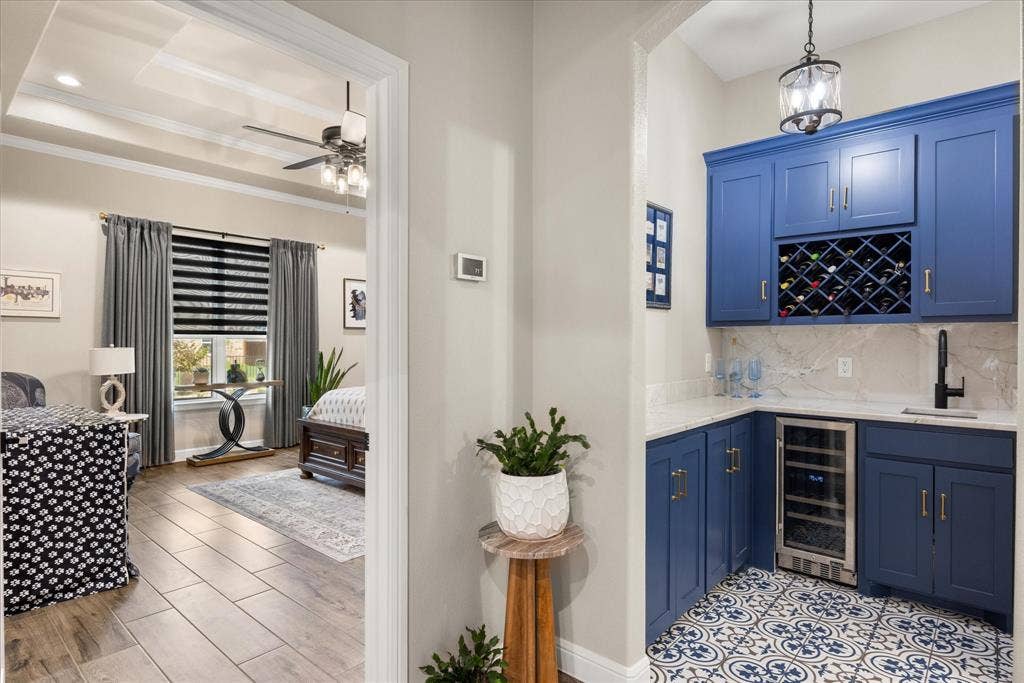 Wet bar featuring custom blue shaker cabinetry, built-in wine rack, stone-finish countertops, decorative patterned tile flooring, and a stainless steel beverage refrigerator