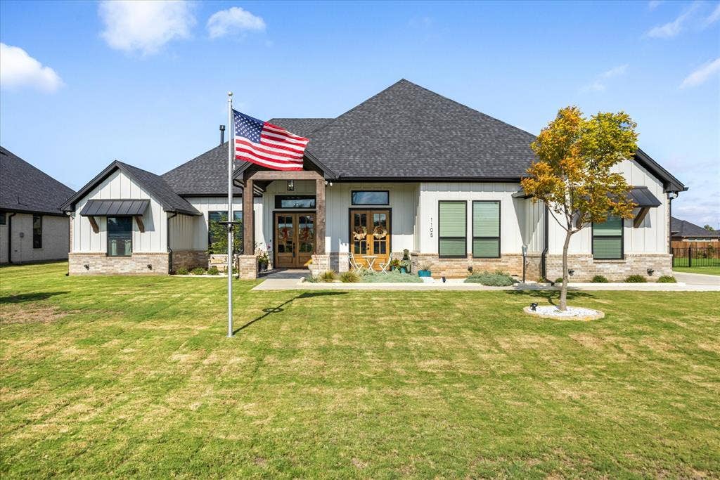 Modern farmhouse exterior featuring vertical board-and-batten siding, stone masonry accents, dual wood-framed entry doors, and dark metal roof detailing