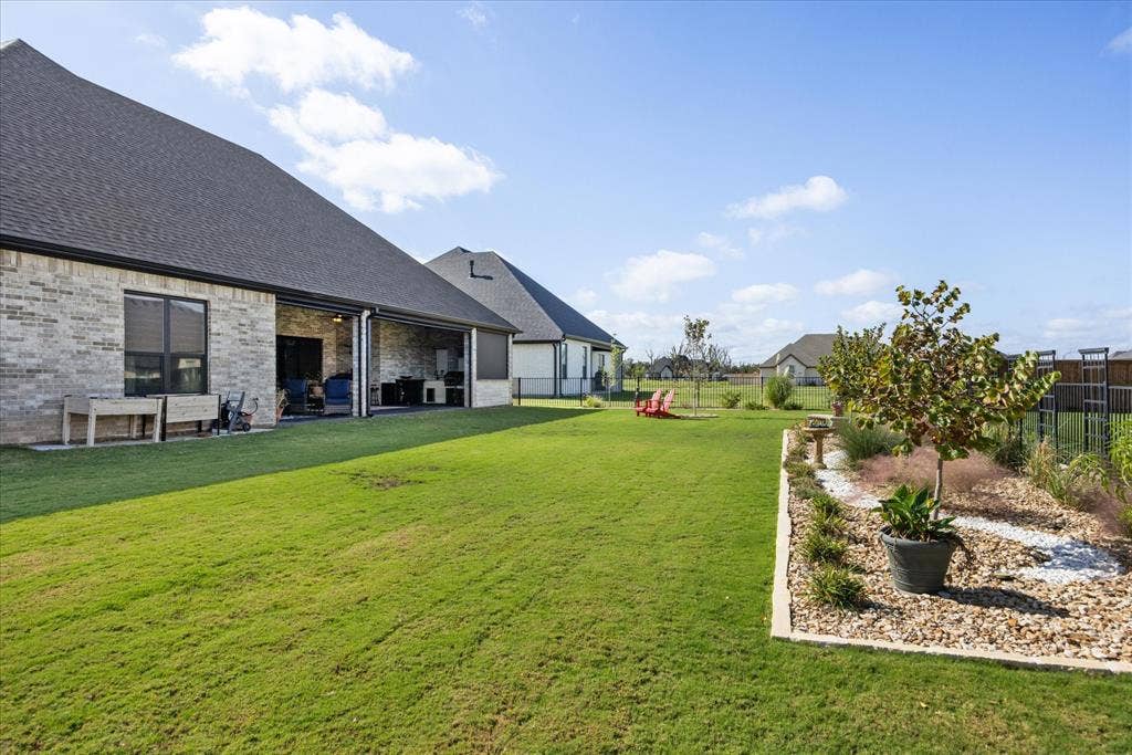 Rear exterior featuring a brick facade, covered patio, manicured lawn, and landscape bed with stone borders
