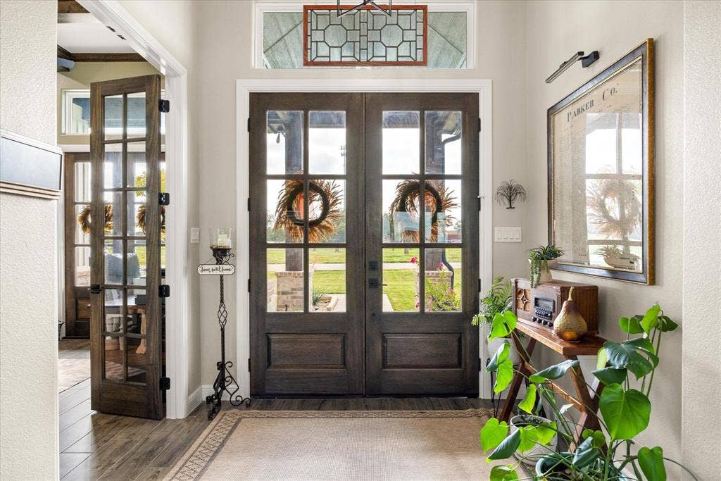 Double entry doors featuring glass paneling, topped with a geometric transom window, complemented by wood-finish flooring and a matching French door