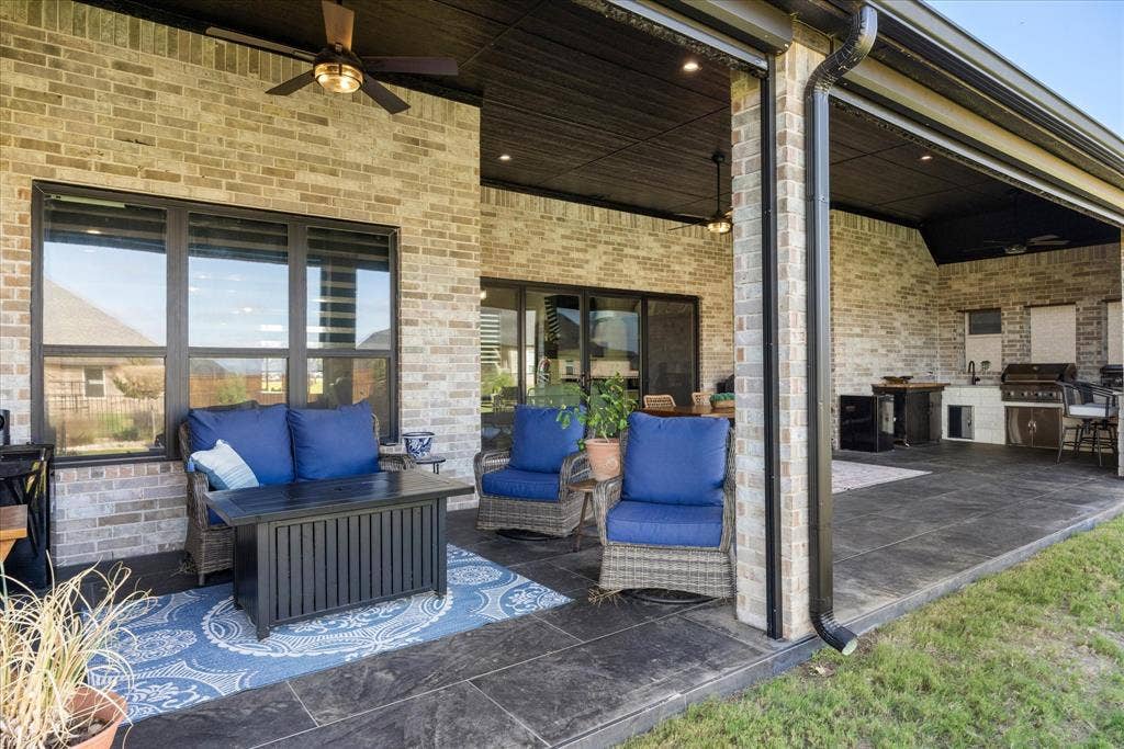 Covered outdoor patio featuring brick exterior walls, tile flooring, built-in outdoor kitchen with grill, and recessed ceiling lighting