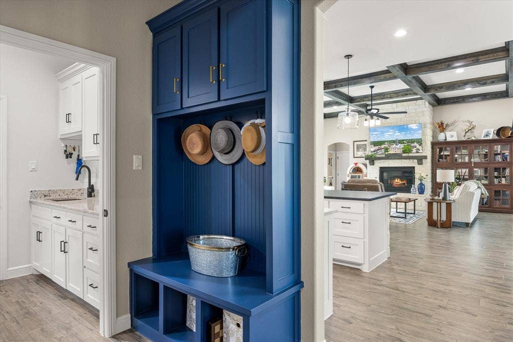 Built-in blue storage cabinetry with gold-toned hardware, wood-finish flooring, custom ceiling beams, and stone-surround fireplace