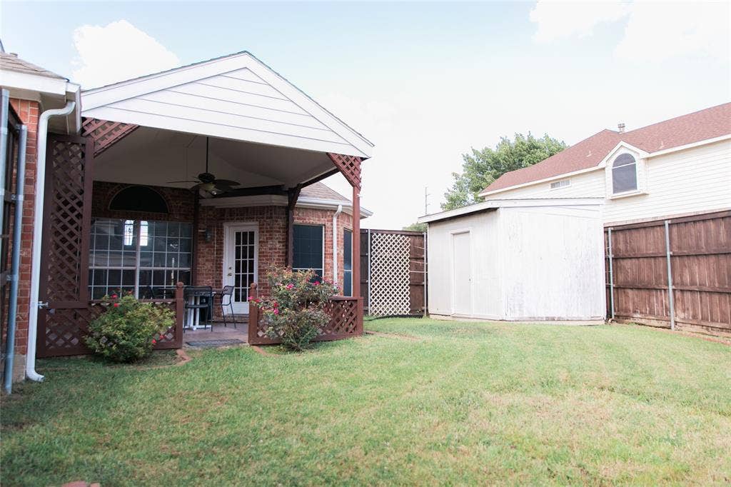 404 Belmont Court, Lewisville, TX 75067 Covered patio featuring a peaked roof, attached ceiling fan, and decorative lattice accents, complemented by a fenced backyard and a standalone storage structure
