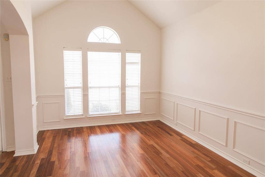 404 Belmont Court, Lewisville, TX 75067 Vaulted ceiling, wood-finish flooring, and white wainscoting complemented by triple-panel windows featuring a prominent arched transom