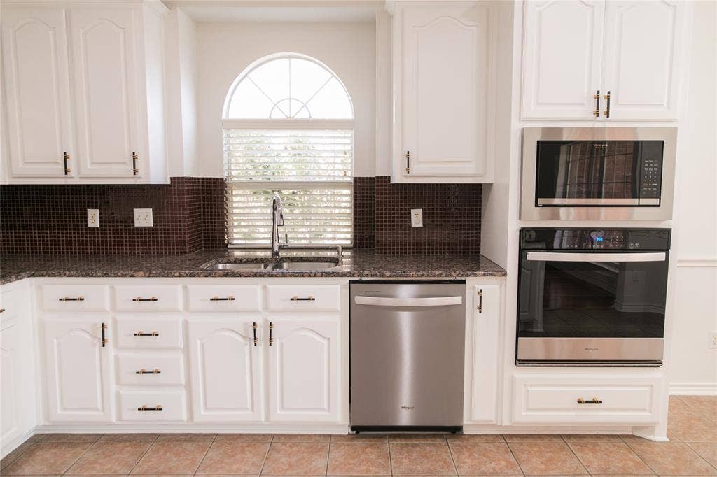 404 Belmont Court, Lewisville, TX 75067 Kitchen featuring white cabinetry, stainless steel built-in double oven and microwave, stone-finish countertops, tiled backsplash, and an arched window