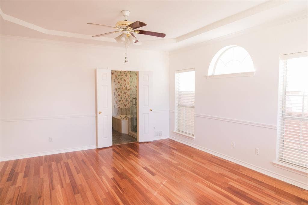 404 Belmont Court, Lewisville, TX 75067 Room featuring wood-finish flooring, tray ceiling, ceiling fan with integrated lighting, dual-pane windows with a fixed arched transom, and chair rail molding