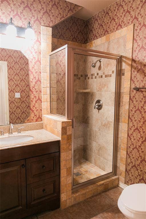 404 Belmont Court, Lewisville, TX 75067 Dark wood-finish vanity with a stone countertop, integrated sink, shower enclosure with tiled surround, and decorative wall covering