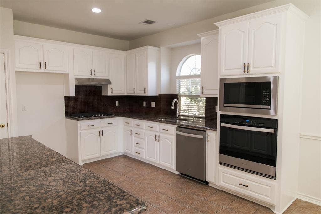 404 Belmont Court, Lewisville, TX 75067 Kitchen featuring white cabinetry, stone-finish countertops, dark tile backsplash, stainless steel built-in double oven and microwave, and an arched window