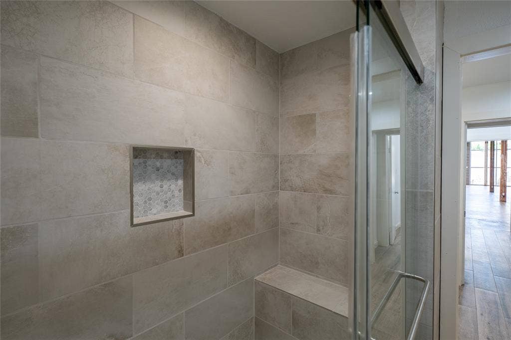 3012 Canton Street, Dallas, TX 75226 Walk-in shower featuring large-format neutral wall tile, integrated tiled bench, inset mosaic-tiled wall niche, and glass enclosure