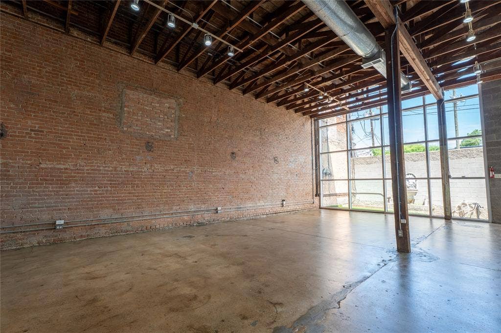3012 Canton Street, Dallas, TX 75226 Industrial-style interior featuring exposed red brick walls, high ceilings with exposed structural beams, polished concrete flooring, full-height glass window wall, and industrial track lighting