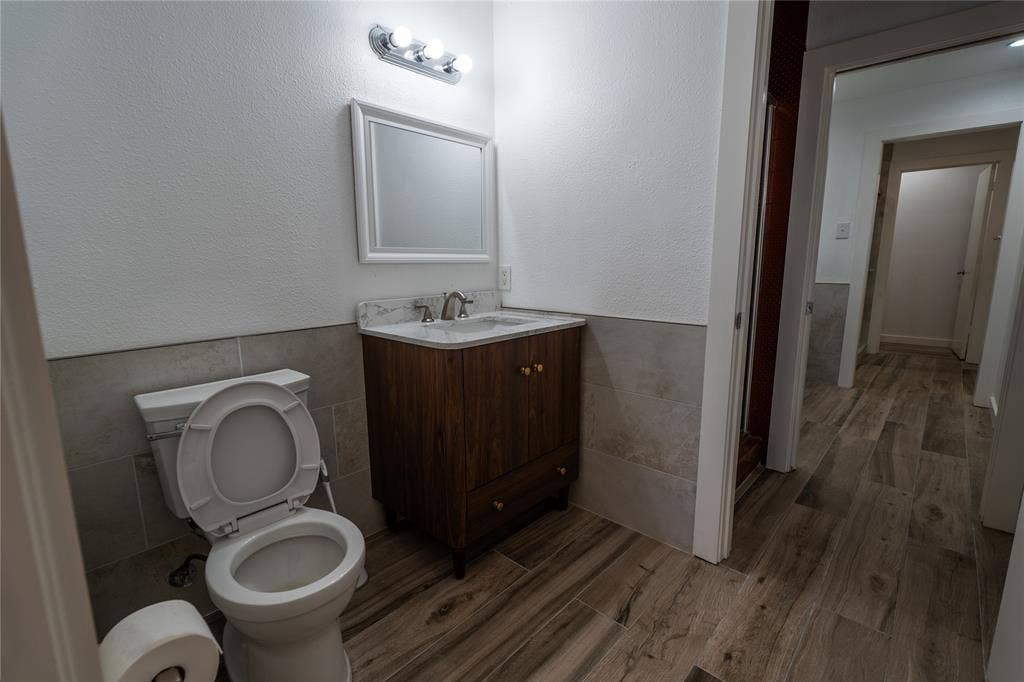 3012 Canton Street, Dallas, TX 75226 Bathroom featuring wood-finish cabinetry, a stone-composite countertop, light-toned wall tile wainscoting, and wood-finish flooring