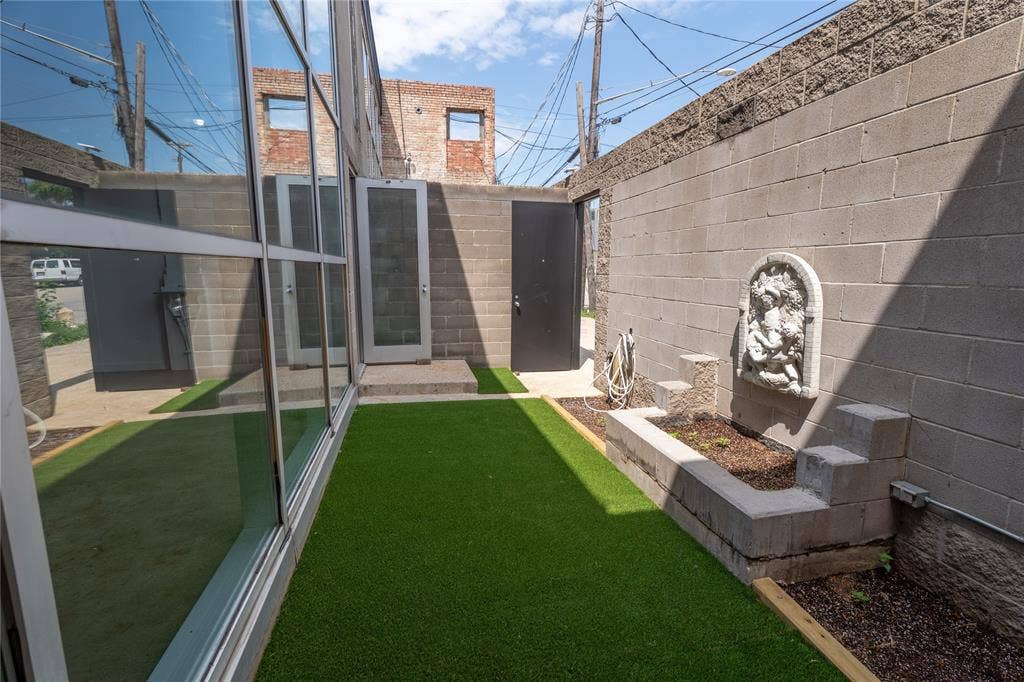 3012 Canton Street, Dallas, TX 75226 Enclosed courtyard featuring full-height glass window walling, concrete masonry unit privacy walls, integrated wall fountain with sculptural relief, and synthetic turf surfacing