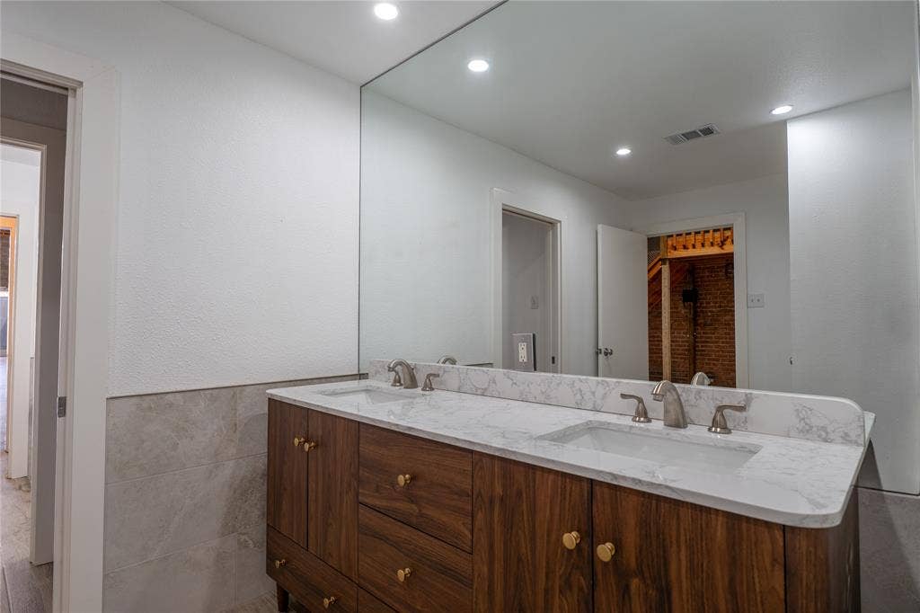 3012 Canton Street, Dallas, TX 75226 Dual-sink vanity with wood-finish cabinetry, stone-composite countertop, full-width wall mirror, and recessed lighting