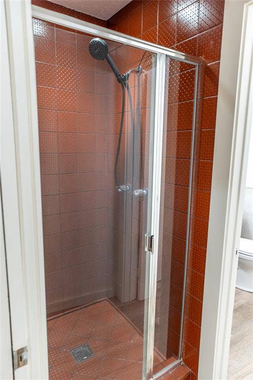 3012 Canton Street, Dallas, TX 75226 Shower stall featuring textured clay-toned wall tiling, a glass-panel door, and a multi-function handheld shower head