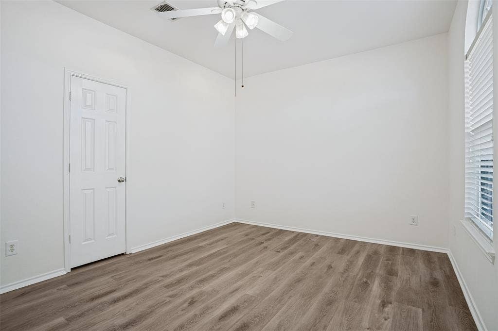 1507 Bankston Drive, Wylie, TX 75098 Room featuring wood-finish flooring, a white ceiling fan with integrated light fixture, a six-panel interior door, and a tall window with horizontal blinds