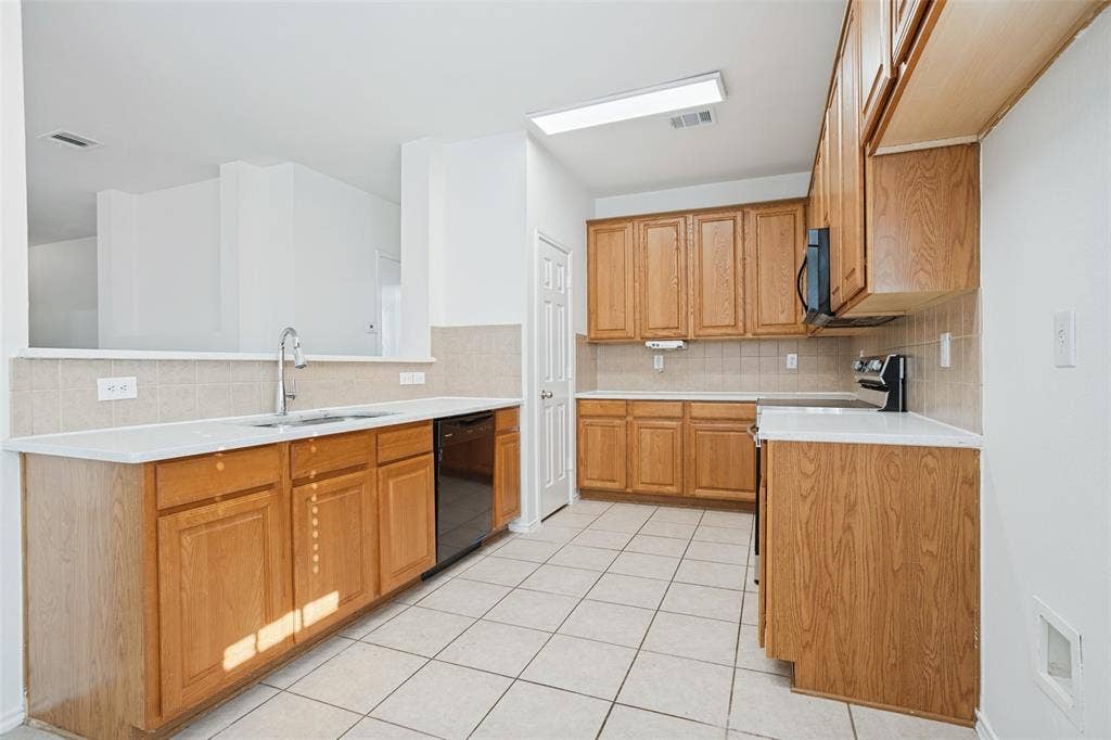 1507 Bankston Drive, Wylie, TX 75098 Kitchen featuring wood cabinetry, solid-surface countertops, tile flooring, a stainless steel undermount sink, and black built-in appliances