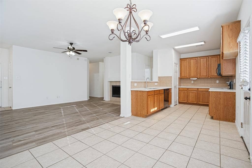 1507 Bankston Drive, Wylie, TX 75098 Kitchen featuring wood cabinetry, ceramic tile flooring, and a stainless steel sink with a goose-neck faucet, complemented by a living area with wood-finish flooring, a fireplace, and a decorative chandelier