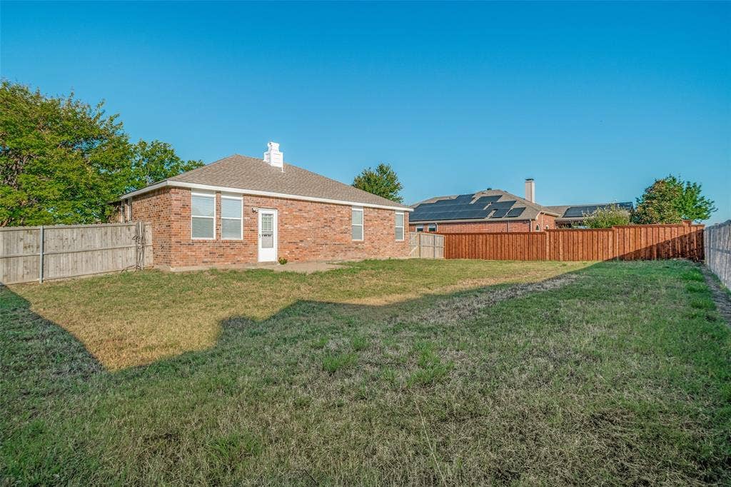 1507 Bankston Drive, Wylie, TX 75098 Rear brick exterior featuring a hip roof, chimney, and expansive lawn enclosed by wood privacy fencing