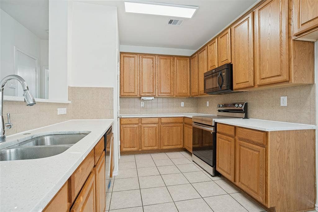 1507 Bankston Drive, Wylie, TX 75098 Kitchen featuring natural wood cabinetry, solid surface countertops, tiled backsplash, stainless steel double-basin sink, and built-in stainless steel appliances