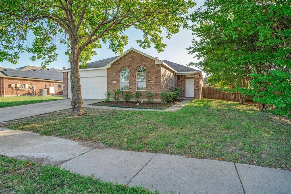 1507 Bankston Drive, Wylie, TX 75098 Brick exterior featuring an arched window design, a concrete driveway, a two-car garage, and mature landscaping