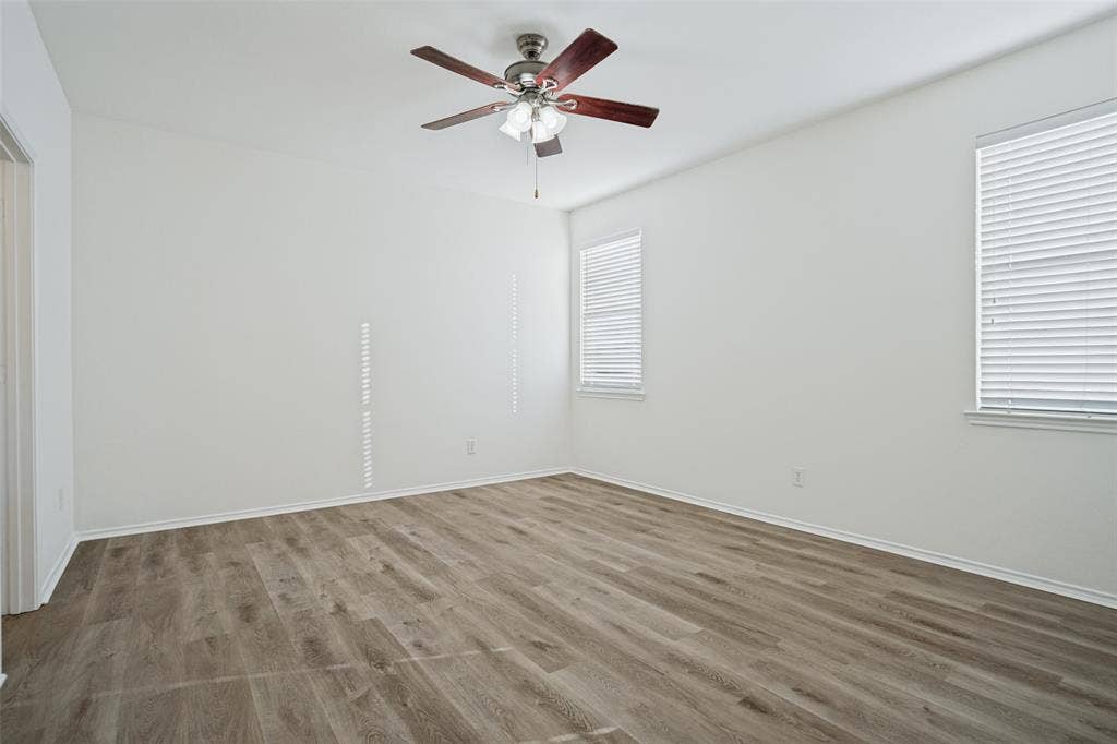 1507 Bankston Drive, Wylie, TX 75098 Neutral-toned room featuring wood-finish flooring, a central multi-blade ceiling fan with integrated lighting, and two windows equipped with horizontal blinds
