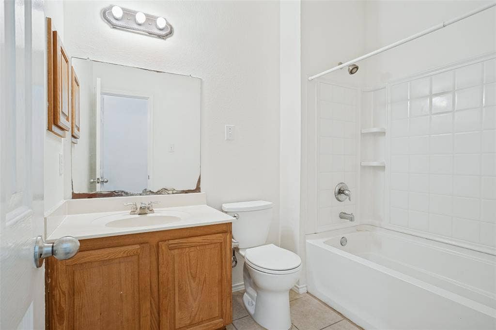 1507 Bankston Drive, Wylie, TX 75098 Bathroom featuring a wood-finish vanity with a composite countertop, integrated sink, wall-mounted mirror, three-light fixture, and a tub-shower combination with tile surround