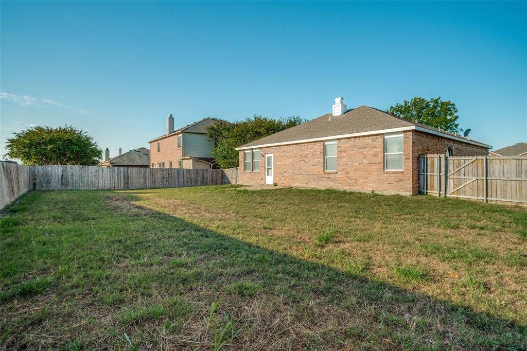 1507 Bankston Drive, Wylie, TX 75098 Rear exterior brick facade with a hipped roofline, chimney stack, and a fenced backyard