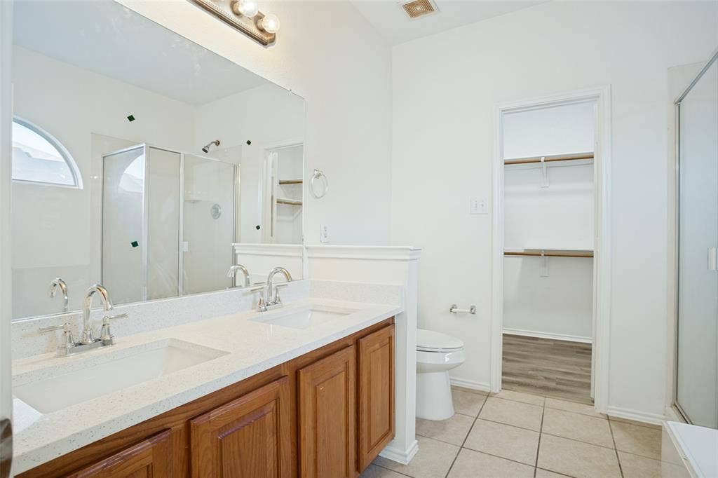 1507 Bankston Drive, Wylie, TX 75098 Dual-sink vanity with light-colored countertops, full-width mirror, glass-enclosed shower, and attached walk-in storage area