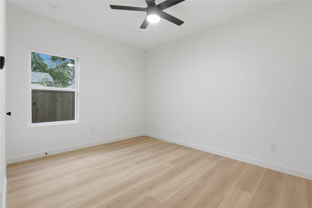 Interior space featuring light-tone wood-finish flooring, neutral walls, a single-pane window, and a matte black ceiling-mounted light fixture with fan blades