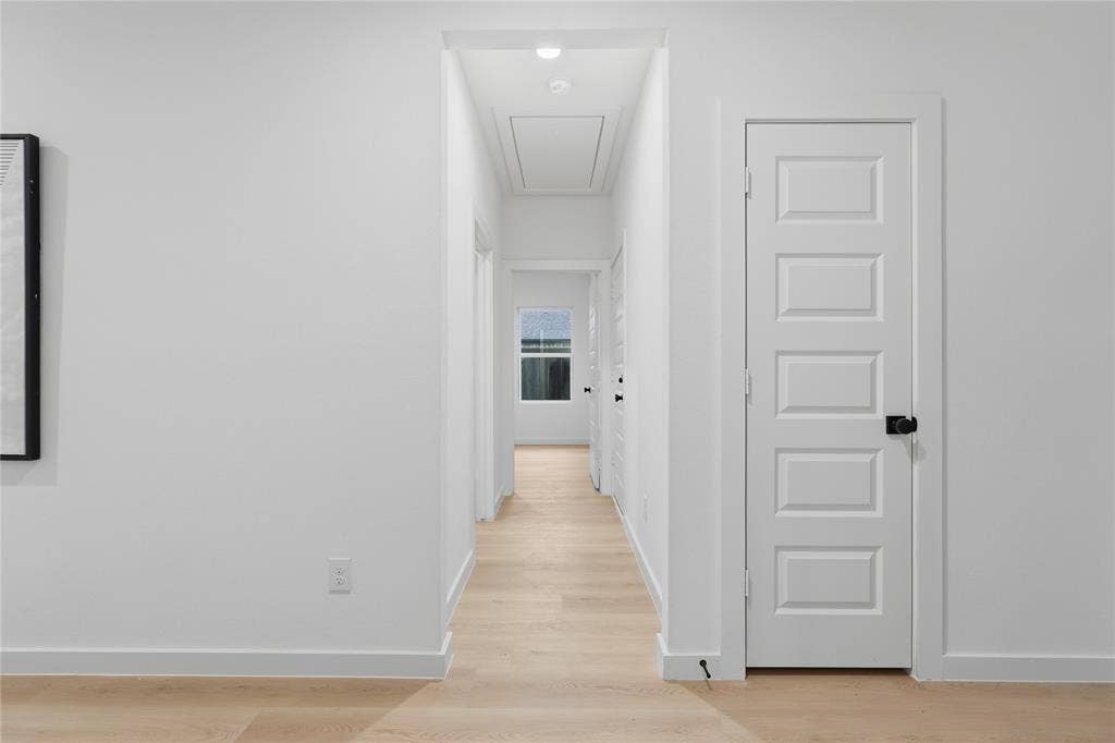 Interior hallway featuring light wood-finish flooring, crisp white walls, five-panel doors, and matte black hardware